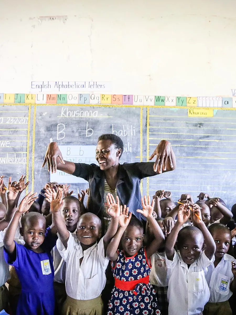 A teacher and her joyful students raise their hands in a bright classroom