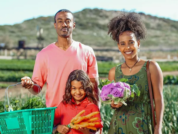 A smiling family holding fresh vegetables on a farm