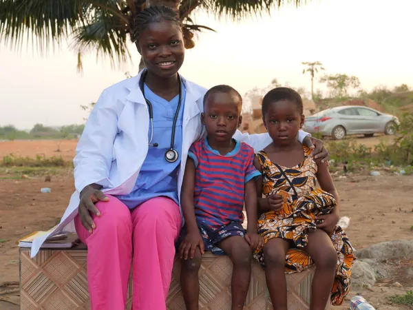 A smiling health worker sitting outdoors with two children