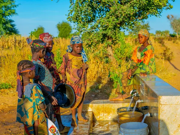Children in colorful clothing gathered at an outdoor water tap