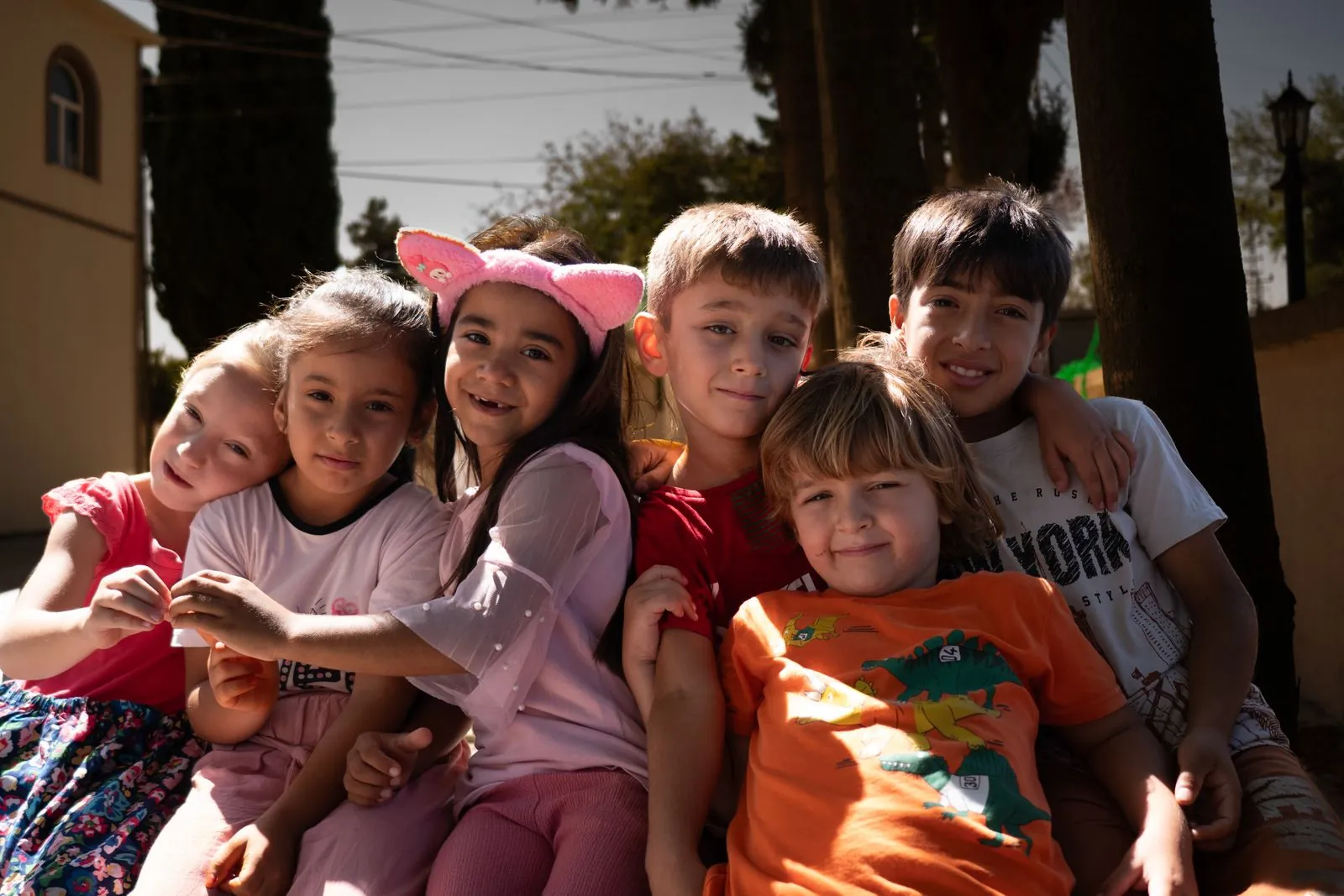 A diverse group of smiling children hugging together outdoors